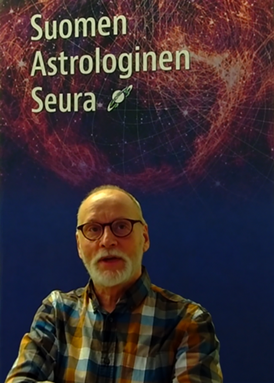 Raimo Nikula luentotallenteessa Suomen Astrologisen Seuran julisteen edessä